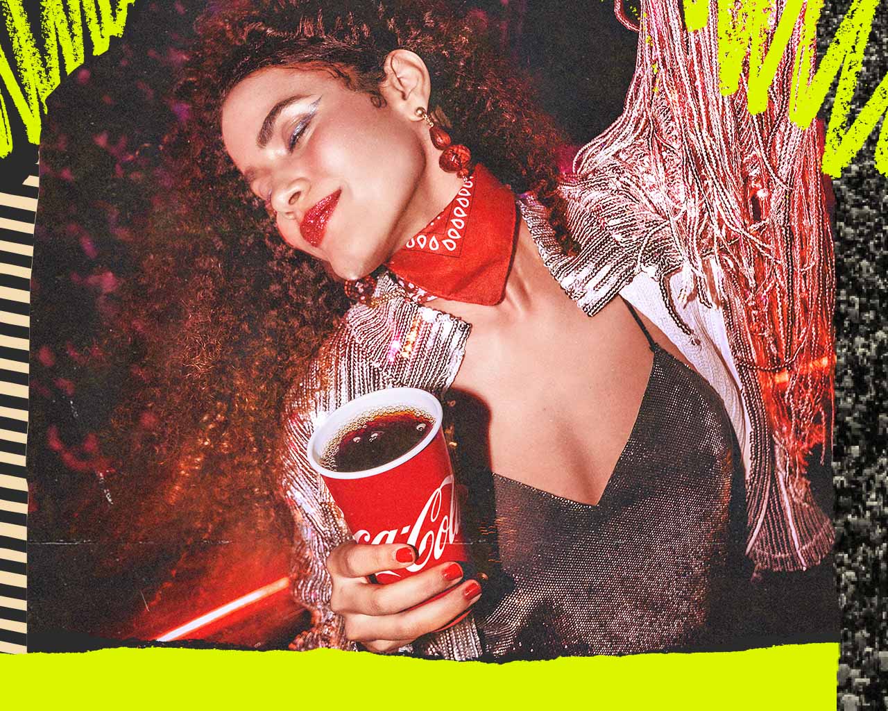 Un grupo de amigos de fiesta por la noche, sosteniendo vasos de Coca-Cola y bailando. Una mujer con el pelo rizado, vistiendo una blusa de patrón floral, está en primer plano riéndose alegremente, rodeada de amigos en un entorno animado y colorido.
