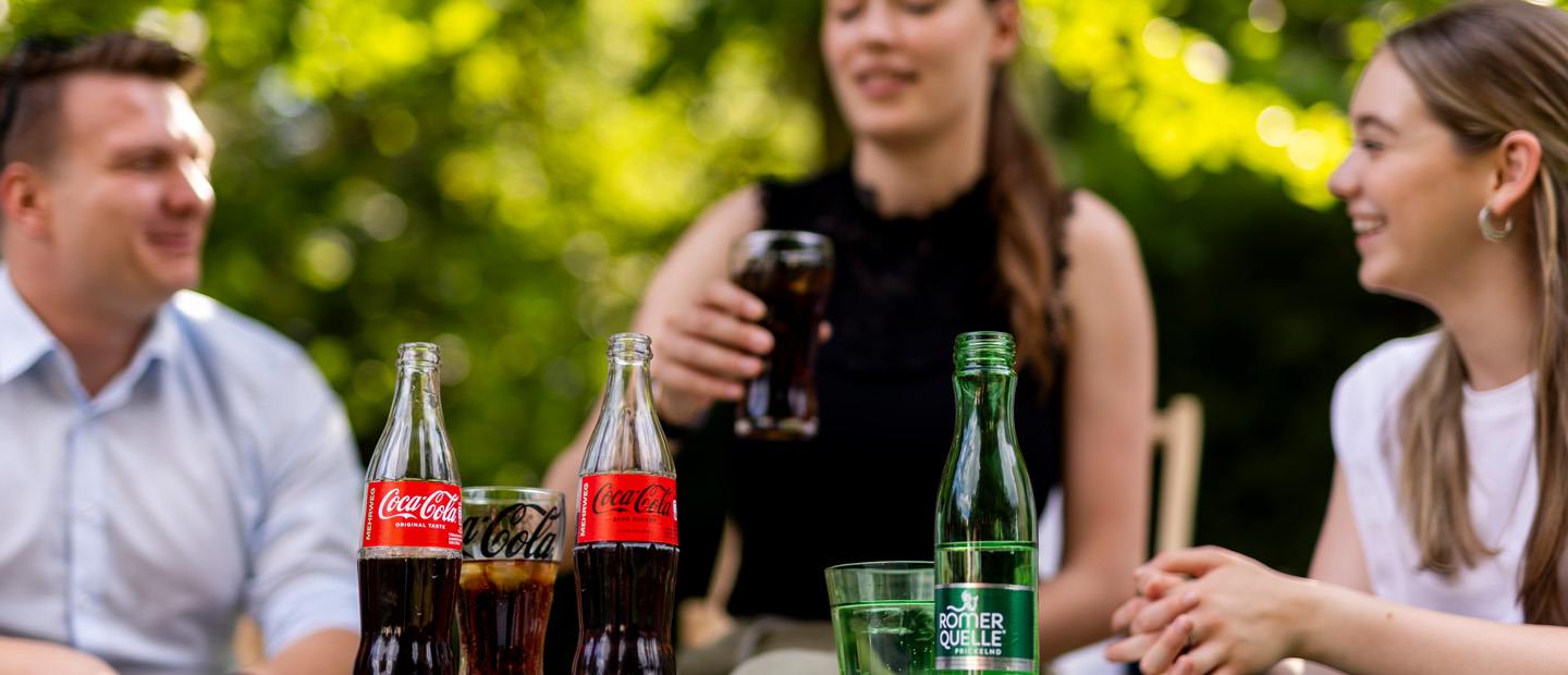 Drei Personen sitzen gemütlich und trinken Coca-Cola