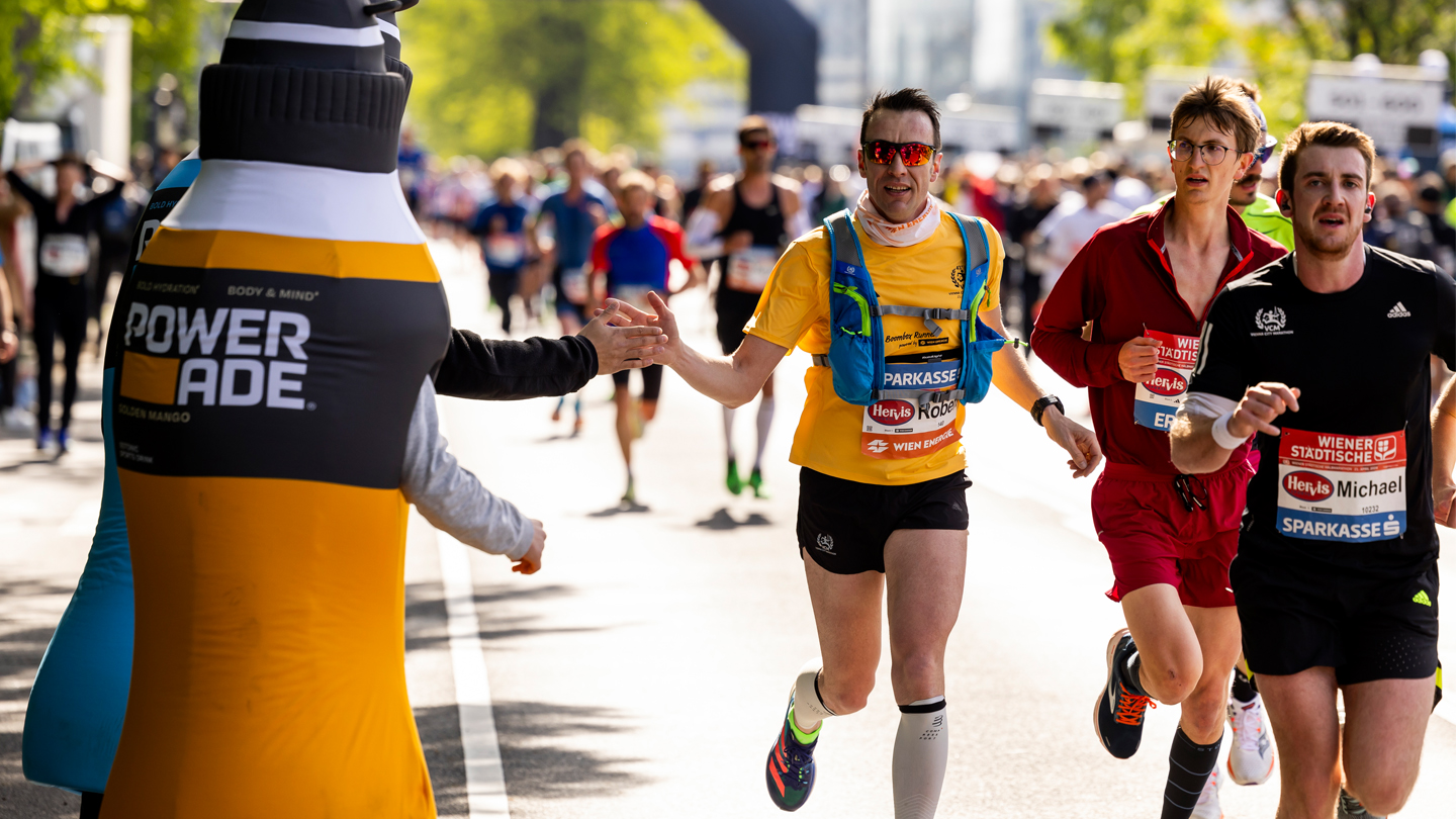Teilnehmer:innen des Vienna City Marathons klatschen bei Powerade Maskottchen ein
