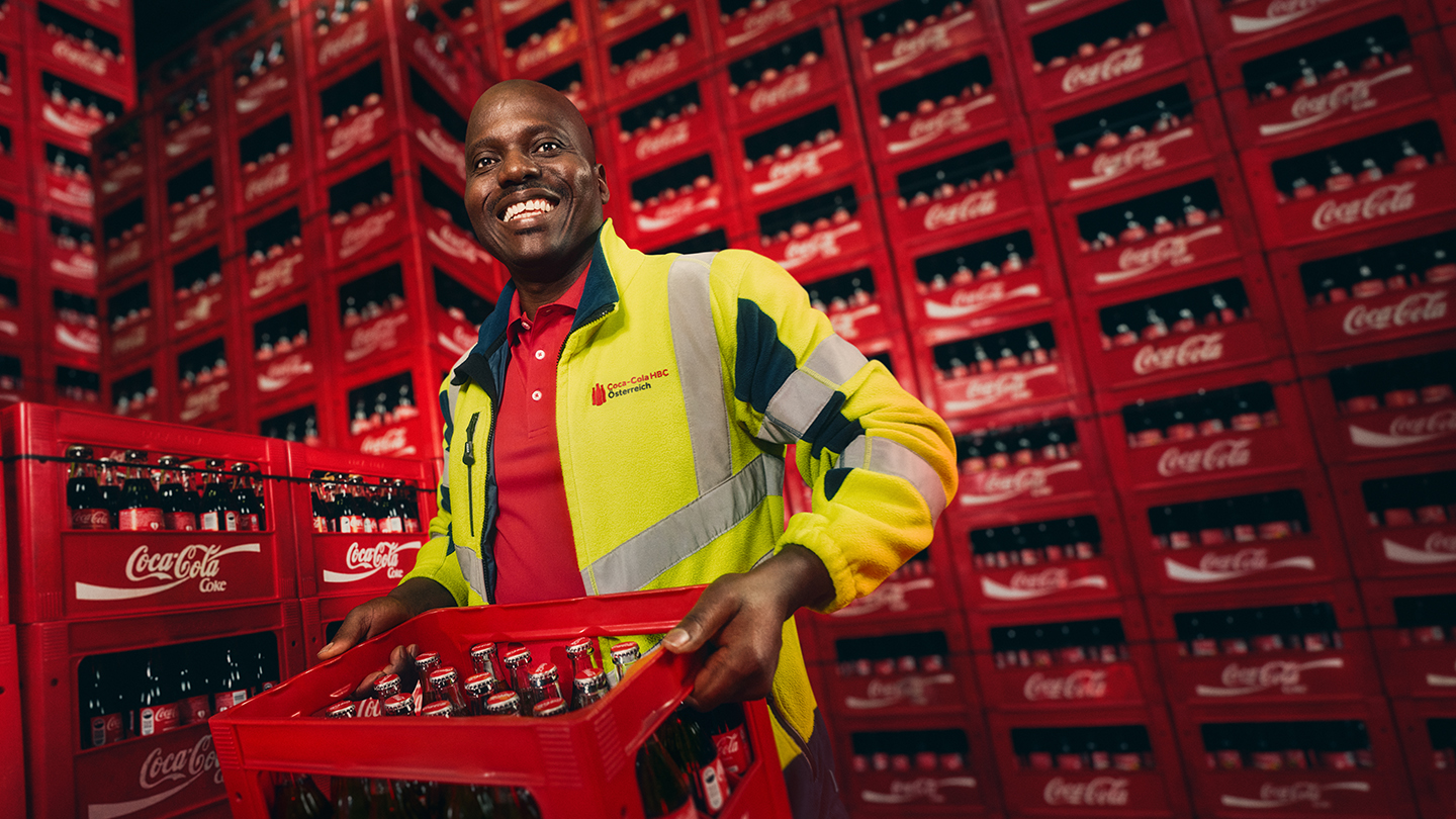 Joe Chinedu transportiert eine Kiste mit Coca-Cola Flaschen im Lager