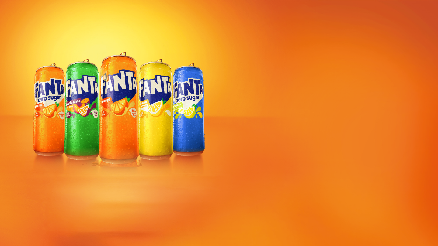 Cinq canettes de Fanta aux couleurs vives (orange, vert, orange clair, jaune et bleu) sont alignées à gauche de l’image, avec des gouttelettes de condensation. Elles sont posées sur une surface orange brillante, devant un large fond dégradé orange et jaune laissant un grand espace vide à droite.