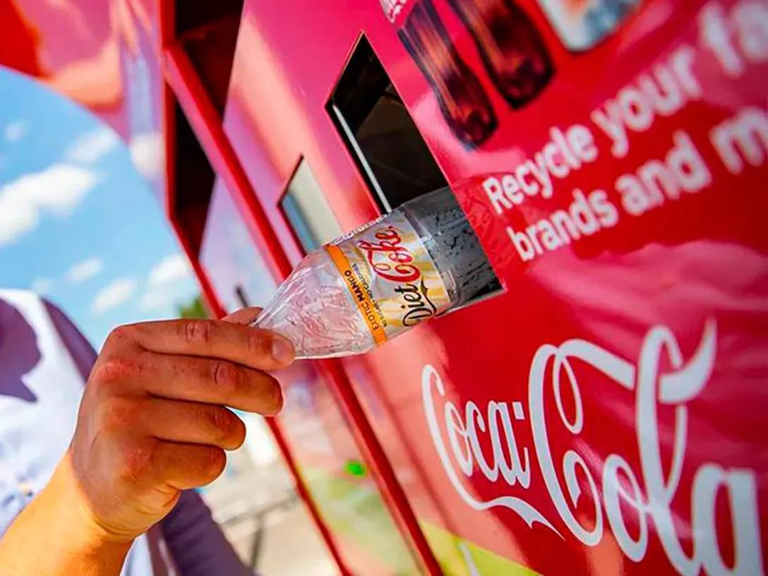 Main déposant une bouteille en plastique Coca-Cola dans une machine de recyclage rouge Coca-Cola