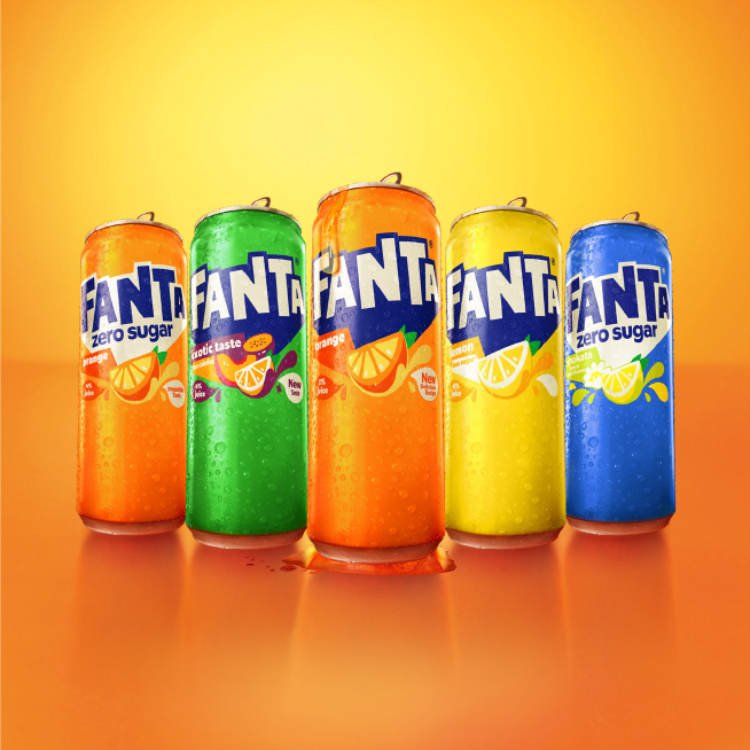 Vijf Fanta‑blikjes in verschillende kleuren en smaken staan naast elkaar tegen een oranje‑gele achtergrond, met zichtbare condensdruppels op de blikjes.
