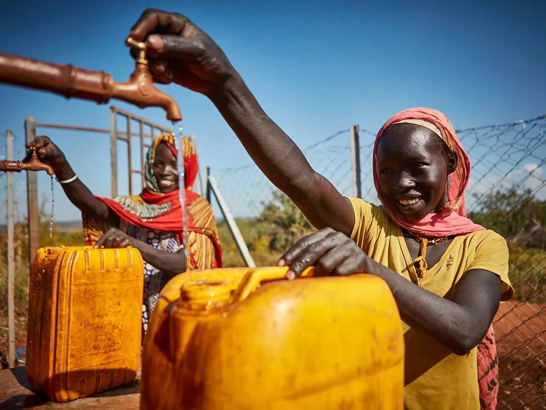 Beeld van twee vrouwen die jerrycans met water vullen in het district Bambasi, in het kader van het Replenish Africa Initiative (RAIN).