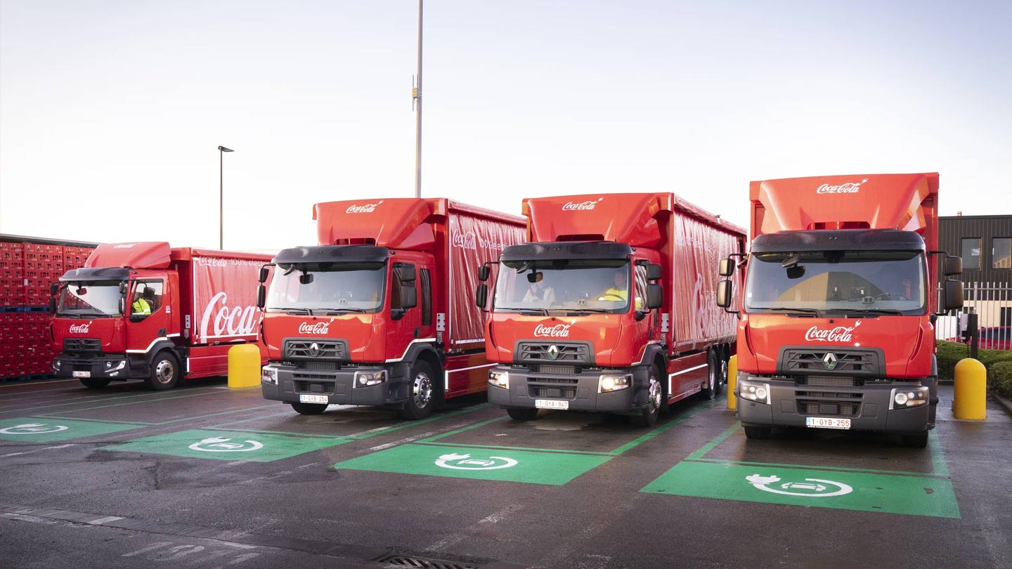Photo de quatre camions rouges Coca-Cola garés dans un parking de rechargement électrique