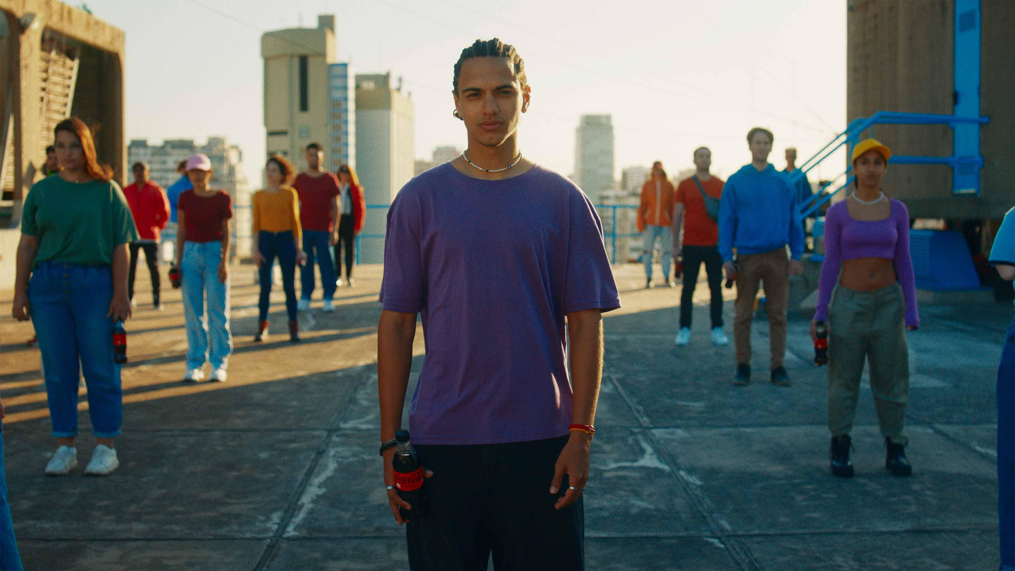 Jóvenes con remeras de distintos colores, están parados mirando hacia adelante, con botellas de Coca-Cola en sus manos