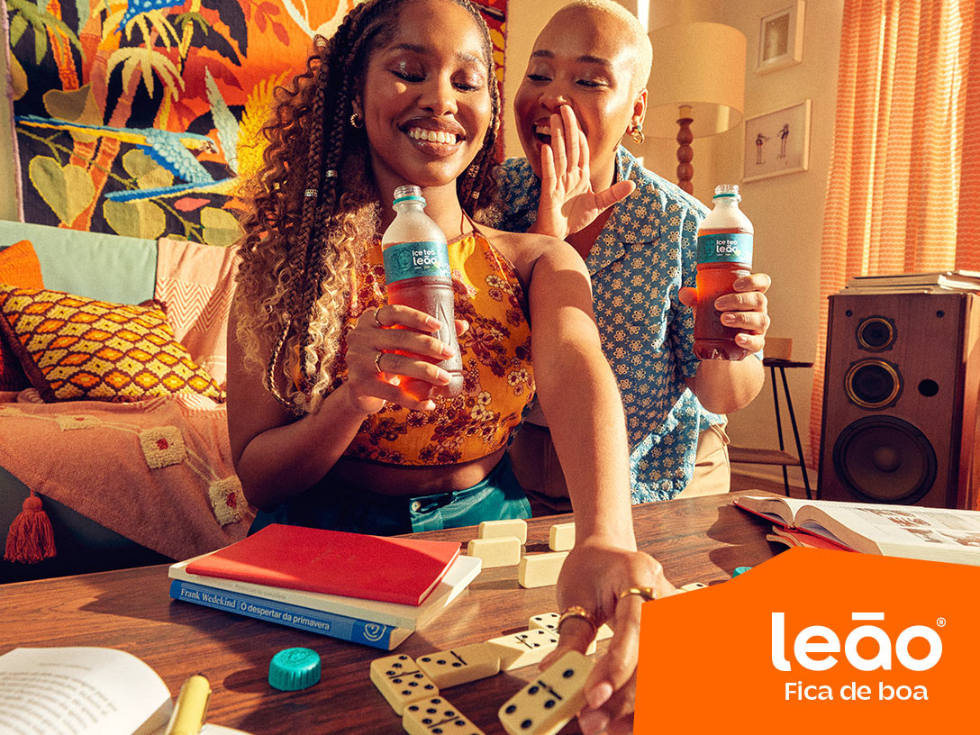 duas mulheres jogando dominó e conversando enquanto bebem um Chas Leão