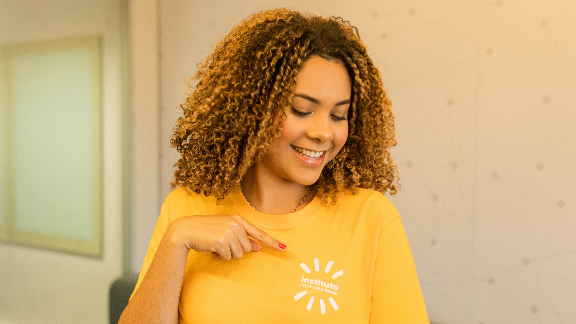Jovem vestindo uma camiseta amarela aponta para o logotipo do Instituto Coca-Cola em sua camisa.