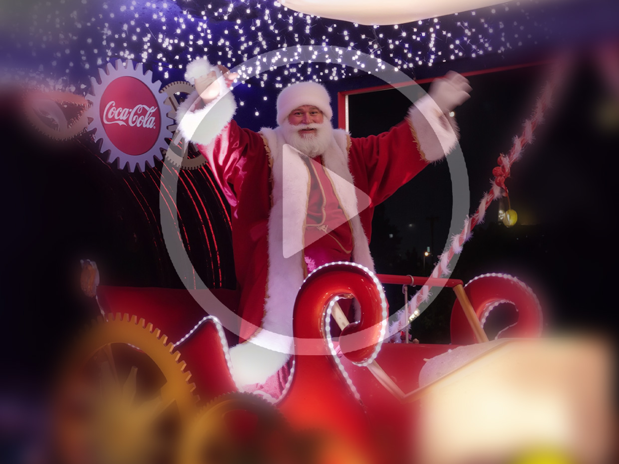 Papai Noel em trenó iluminado, com logo da Coca-Cola e fundo festivo.