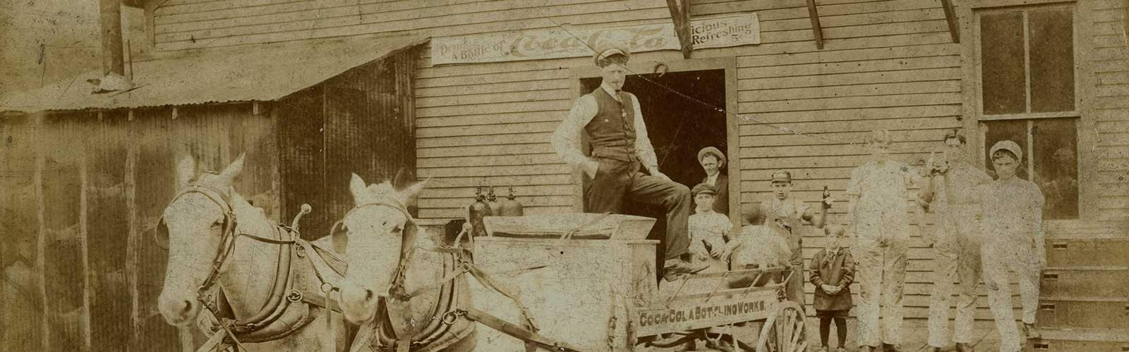 Ein Mann auf einer Pferdekutsche mit Personen am Coca-Cola trinken im Hintergrund