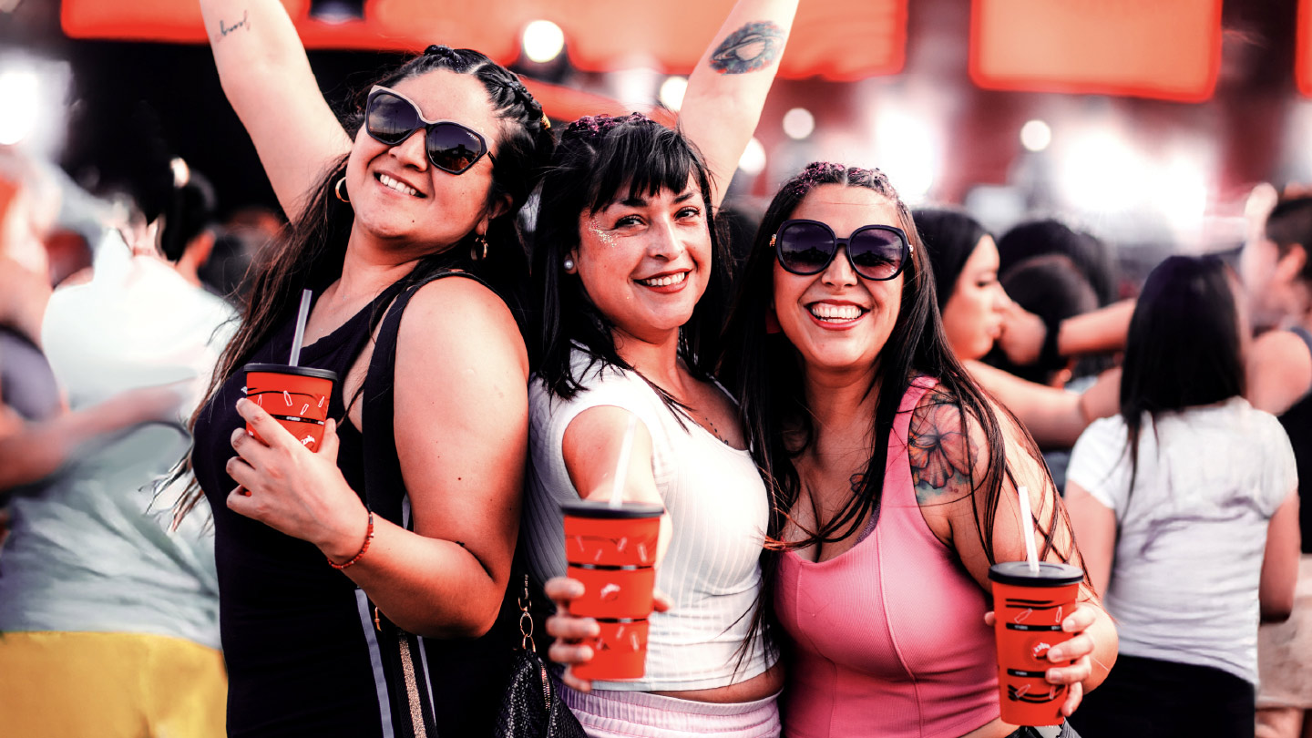 Un grupo de personas disfrutando del festival Maipú de Coke Studio en Chile, sosteniendo vasos rojos con el logo de Coca-Cola. Al fondo, se observan pantallas iluminadas con el logotipo de Coke Studio y luces brillantes que ambientan el evento. La escena refleja un ambiente festivo y lleno de energía.