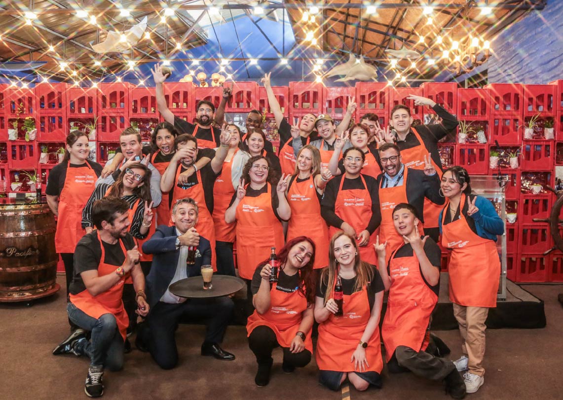 Equipo de trabajo sonriente con delantales naranjos, celebrando juntos en un ambiente festivo.