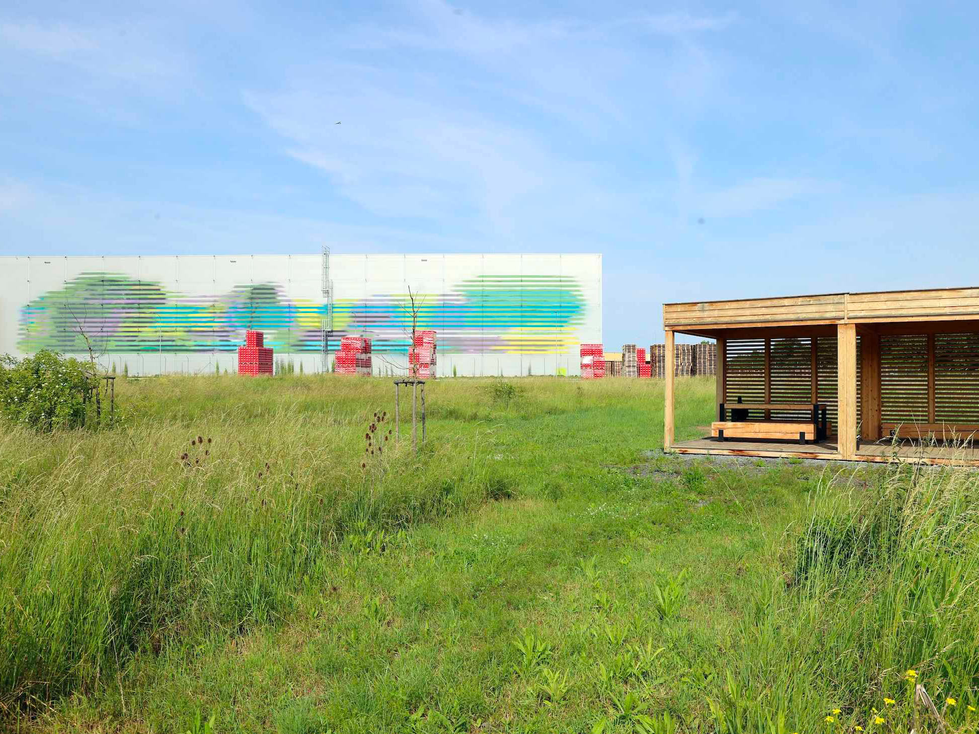 Dřevěný altán na louce s barevnou muralovou stěnou v pozadí.