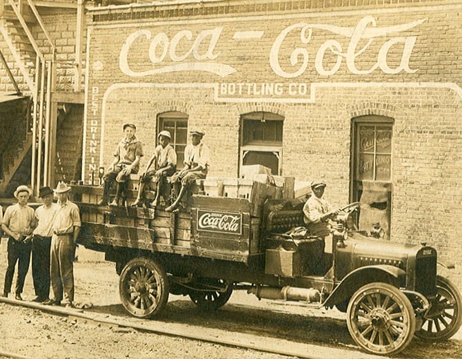 Groupe d’hommes assis sur une voiture avec logo Coca‑Cola
