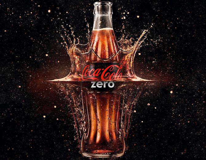 Coca‑Cola Zero pudel, mille ümber pritsib mullitav jook mustal taustal.