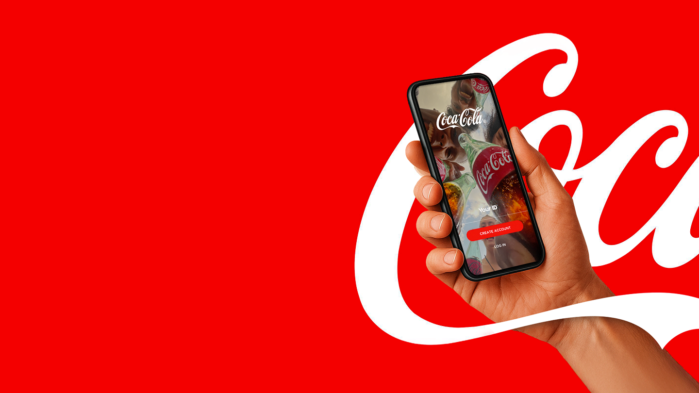 En hånd holder en smartphone med Coca‑Cola‑appen på en rød baggrund.