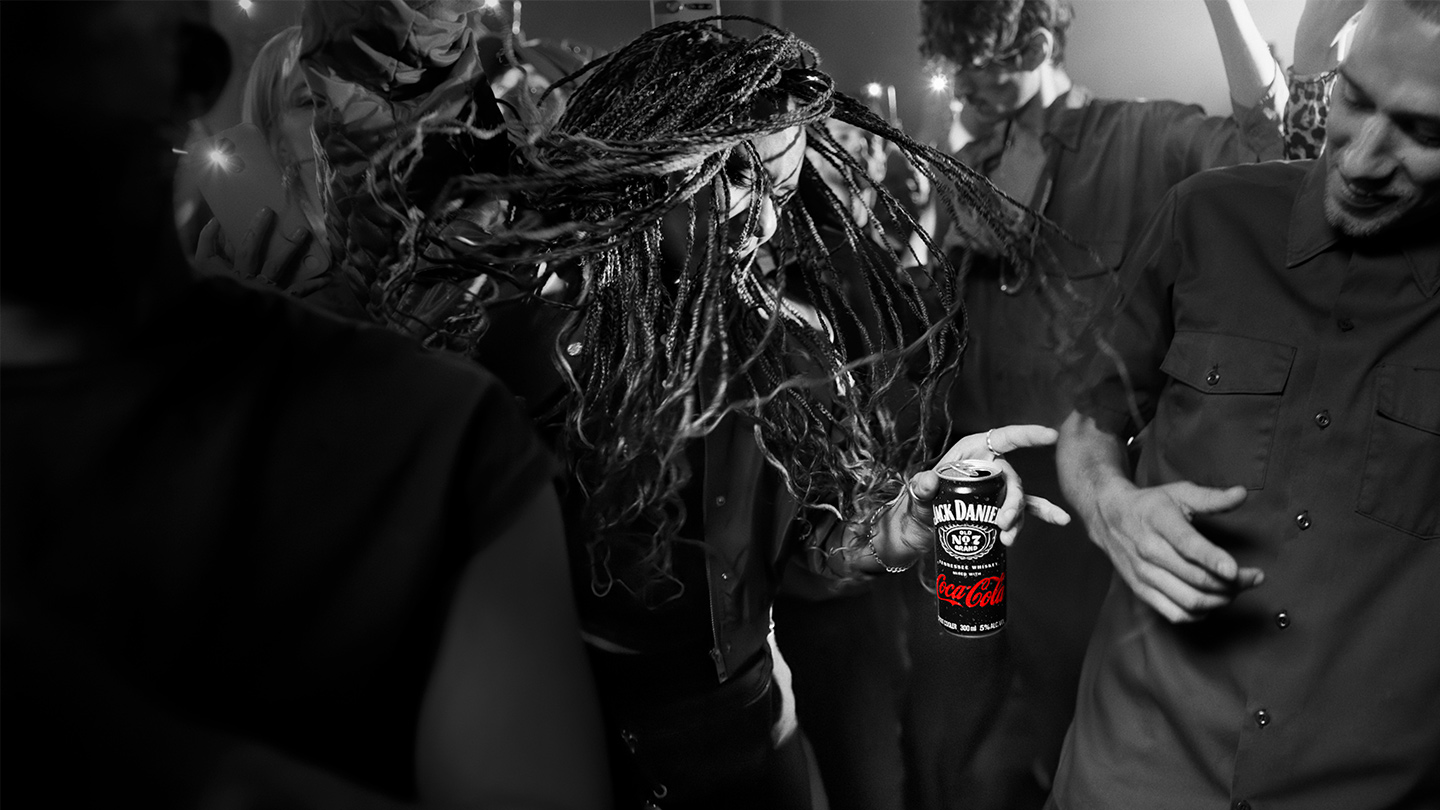 Person duke mbajtur një kanaçe Jack Daniel’s dhe Coca-Cola në një ambient feste.