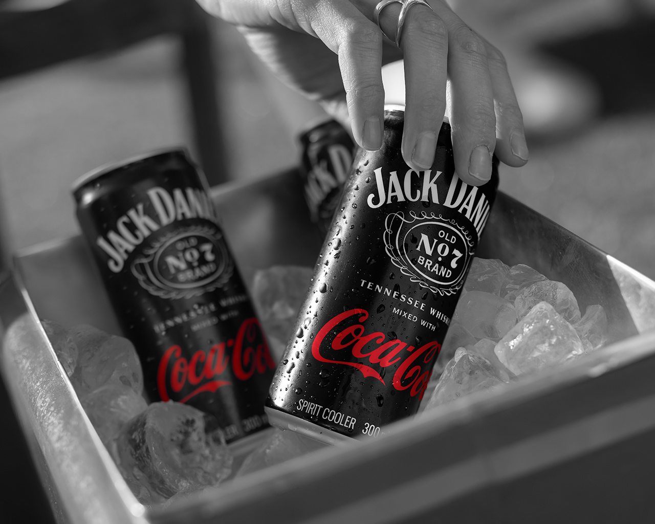Dorë duke marrë një kanaçe Jack Daniel’s dhe Coca-Cola nga një kuti me akull, me një kanaçe tjetër në sfond.