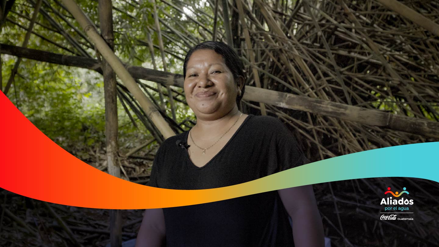 Mujer sonriendo, de fondo una selva con plantas de caña