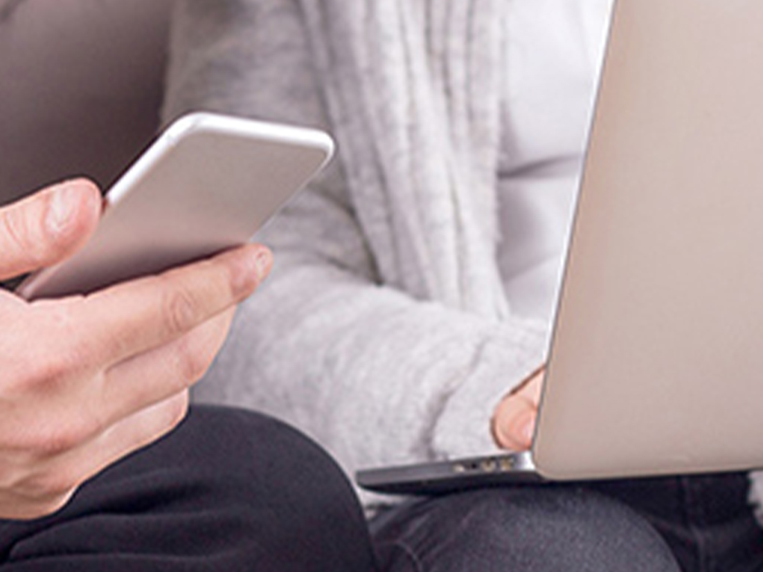 スマホを持つ手とノートパソコンで作業する手