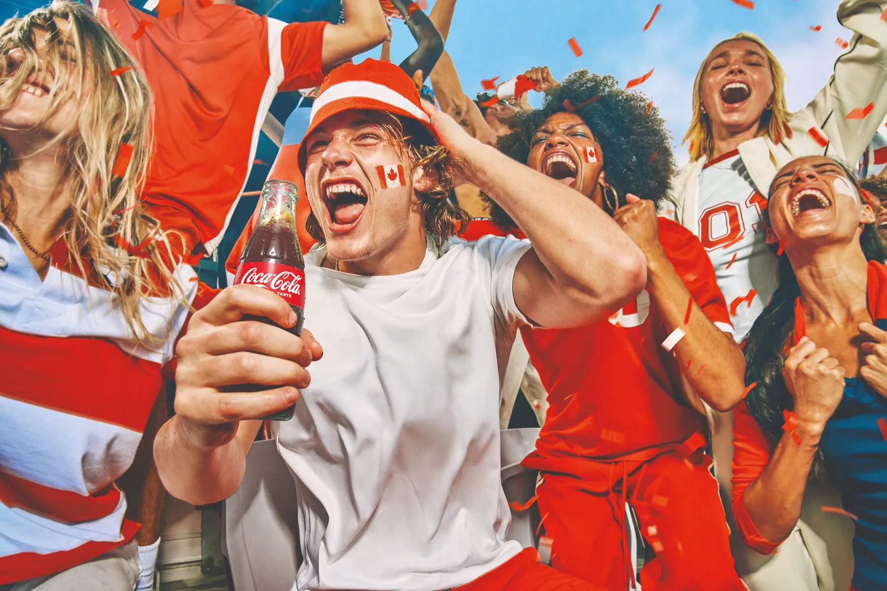 축구 팬들이 코카-콜라를 들고 신난 표정으로 FIFA 월드컵 경기를 열정적으로 응원하는 모습.