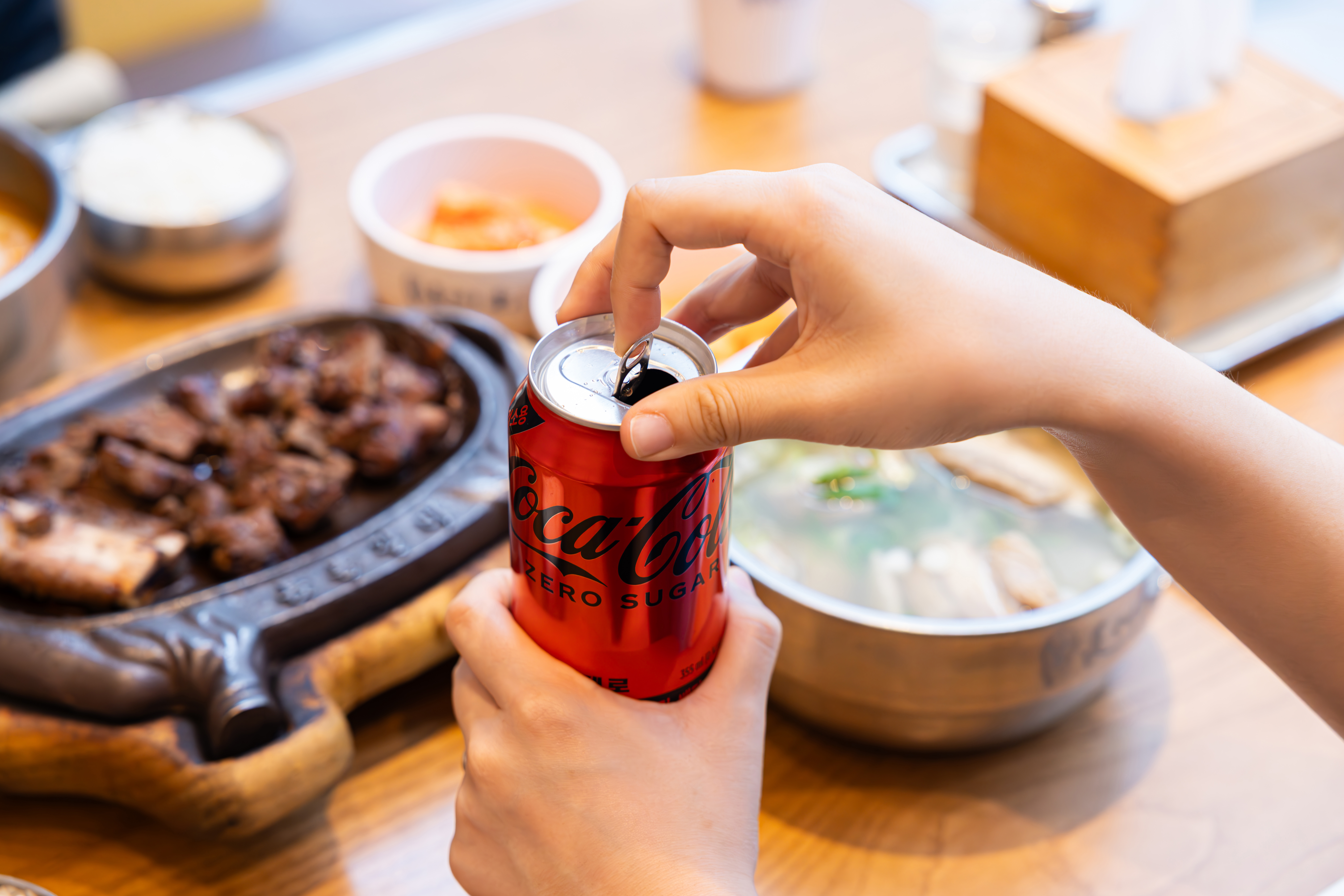 장수갈비집본가의 대표 메뉴들과 코카-콜라 제로 캔을 따고 있는 사진