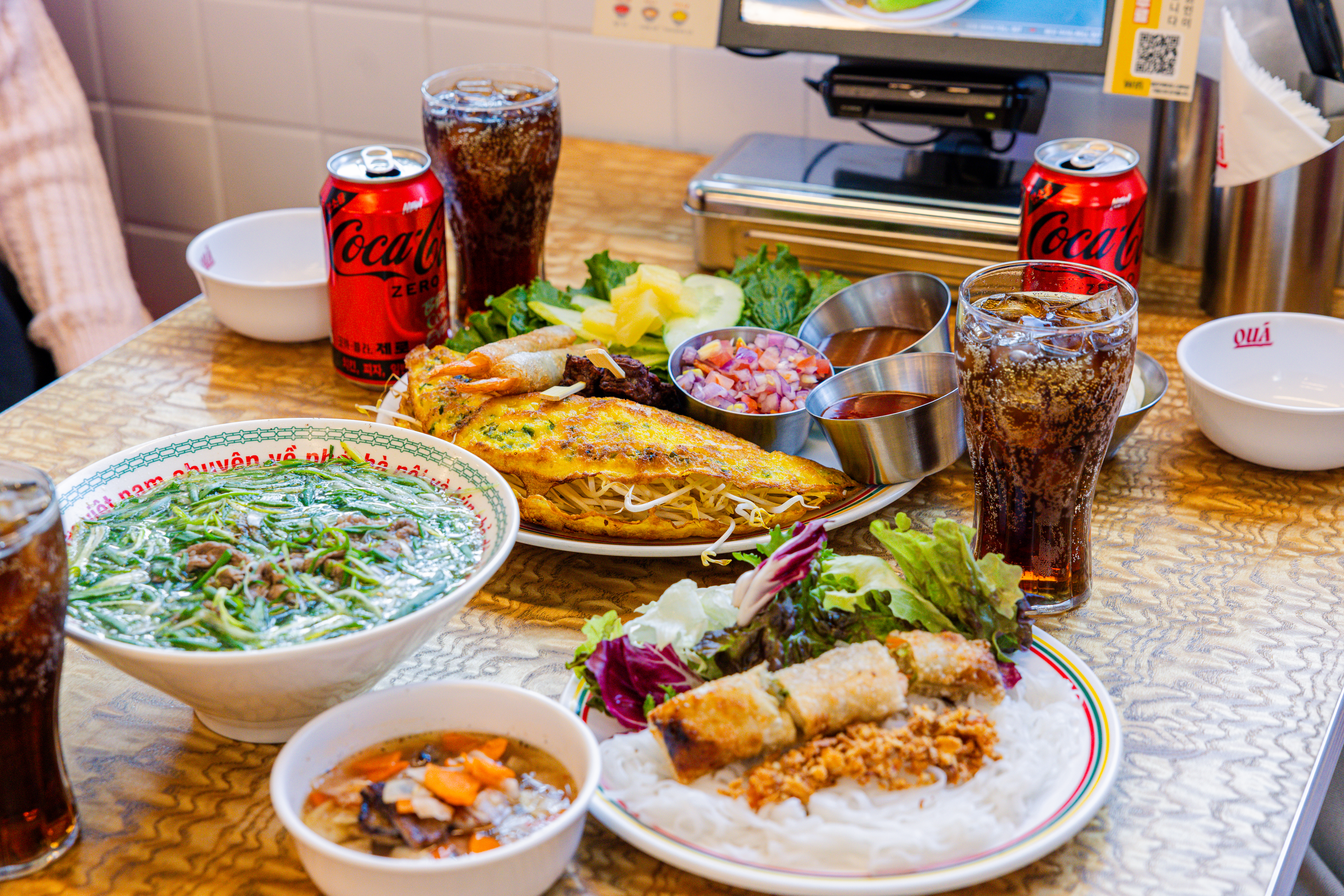 '꾸아 성수본점'의 대표메뉴, 한우사골직화칼국수, 1인 분짜, 냐짱반세오를 코카-콜라 제로와 함께 즐기고 있다.