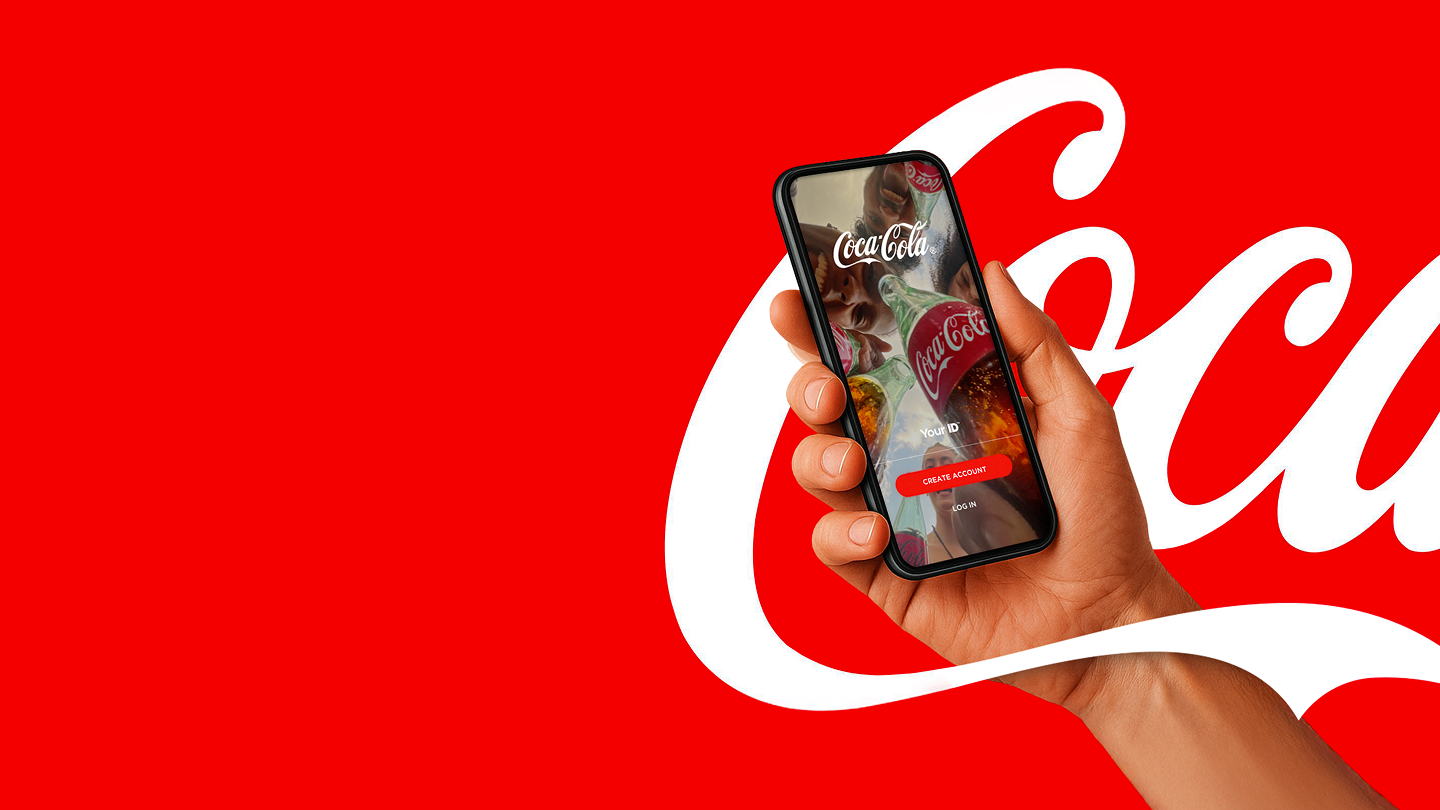 O mână ține un smartphone cu aplicația Coca‑Cola pe un fundal roșu.