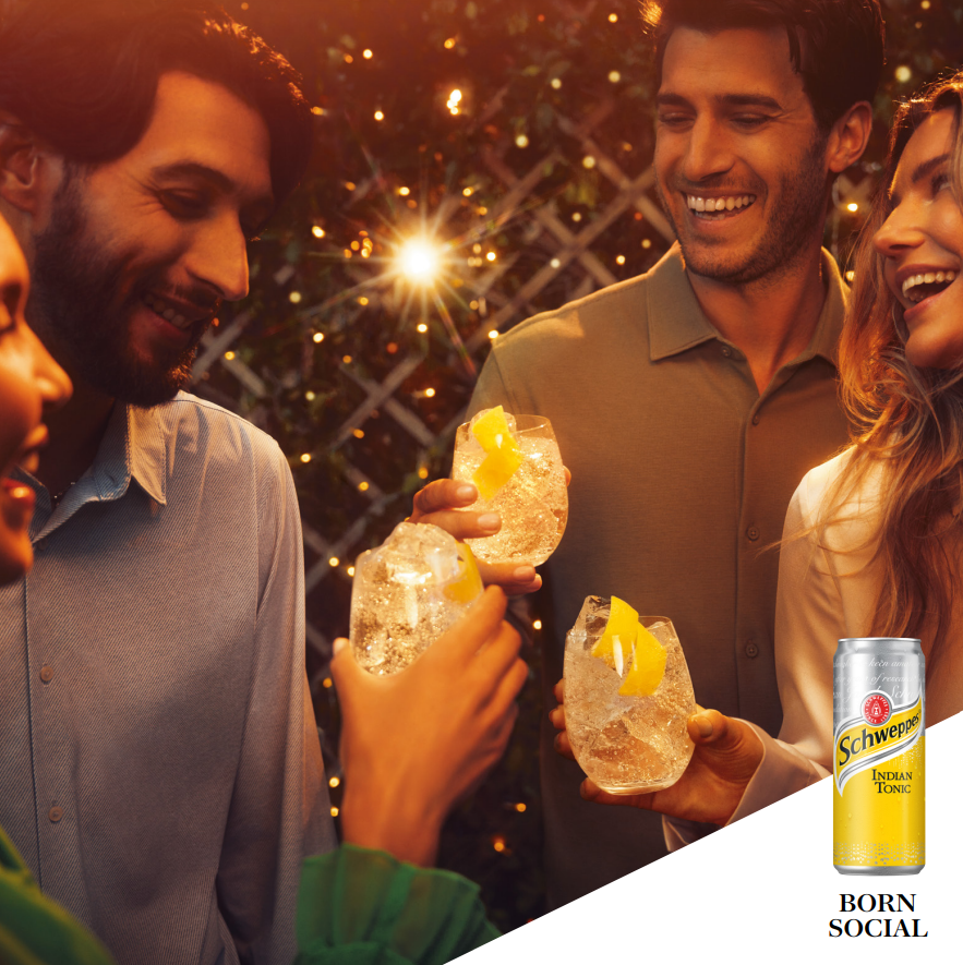 Oameni savurând băuturi Schweppes în aer liber la apus