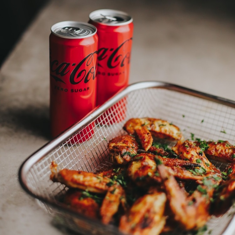 Kosh me krahë pule të pjekur me erëza para dy kanaçeve Coca-Cola Zero Sugar.