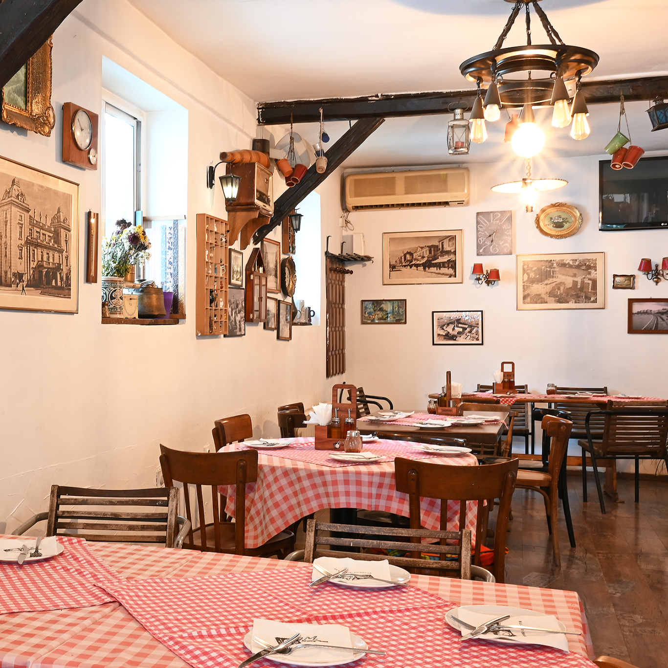 Brendësia e një kafeneje me tavolina druri dhe mbulesa tavoline me kuadrate të kuqe dhe të bardha.