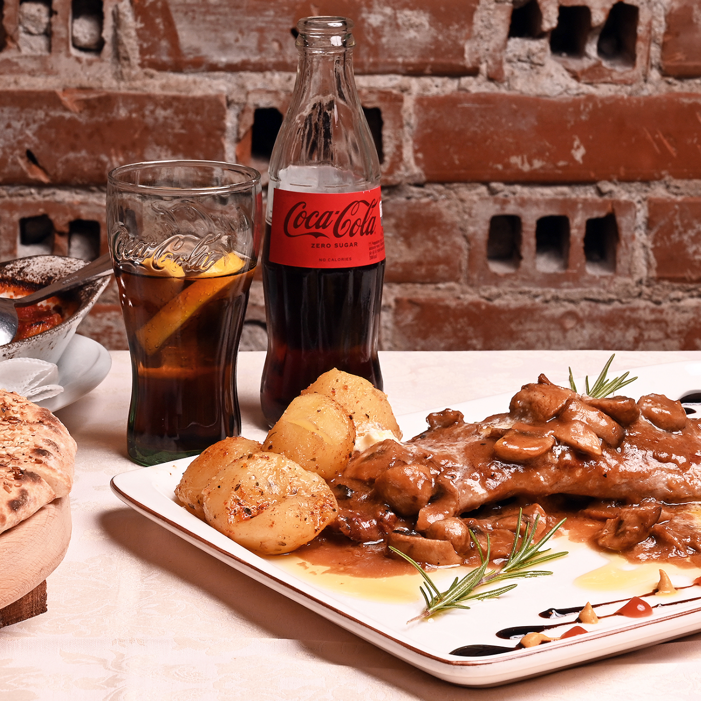 Pjatë me mish me kërpudha dhe patate, me gotë dhe shishe Coca-Cola Zero.