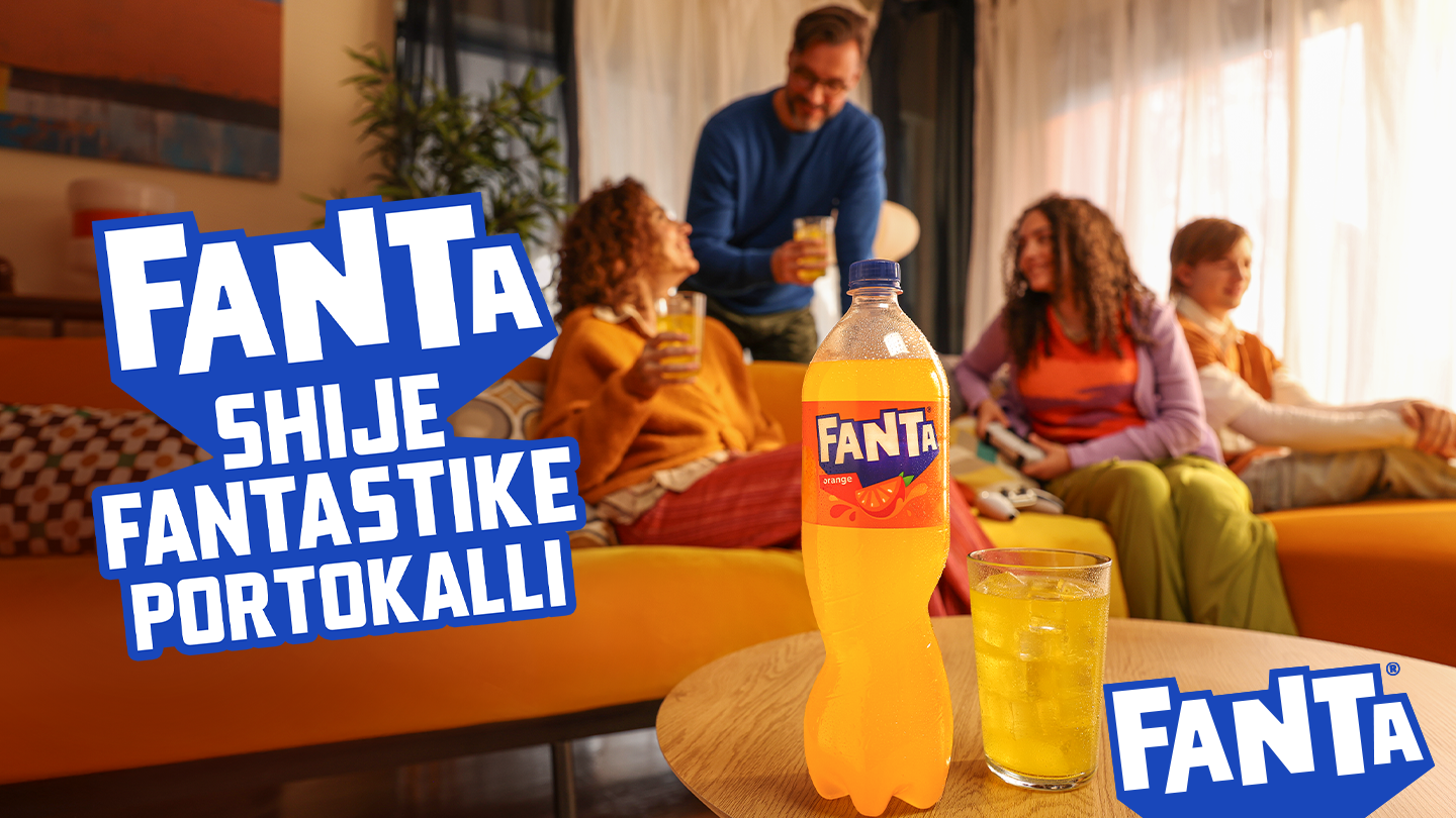 Familja është ulur në dhomën e ndenjës, luan video‑lojëra dhe shijon pijen, ndërsa shishja e Fantës me portokall është e theksuar në plan të parë si simbol i momenteve të përbashkëta dhe shijes së shkëlqyer.
