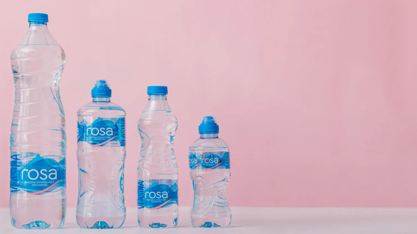 Katër shishe uji Rosa me madhësi të ndryshme në sfond rozë.