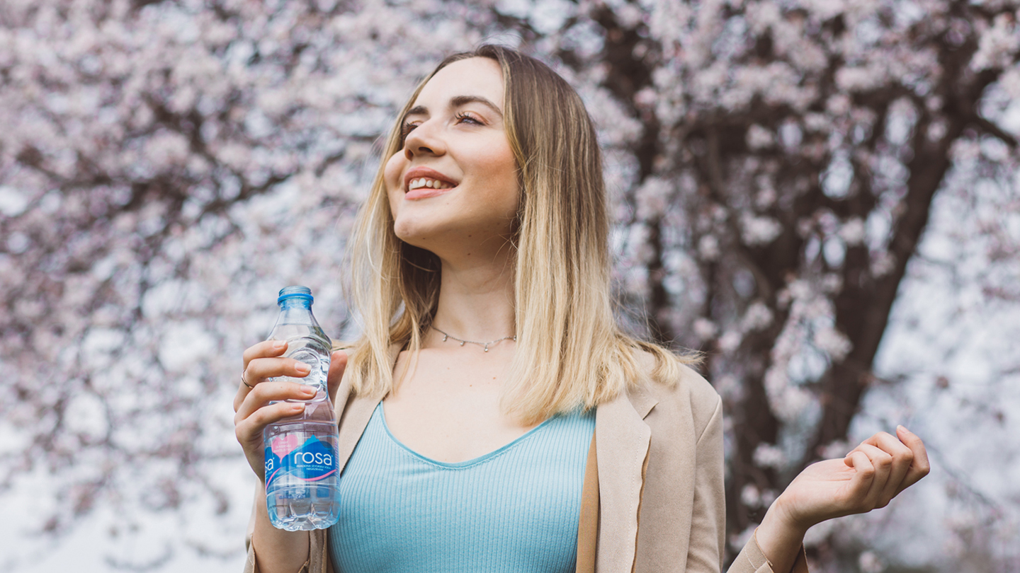 Person mban shishe të vogël uji Rosa para pemëve me lule.