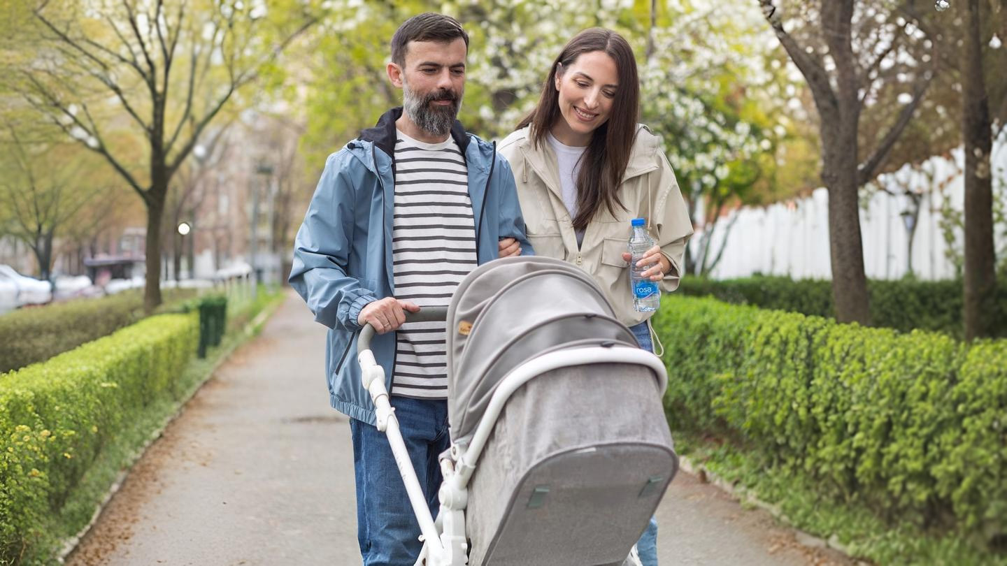 Dy persona shëtisin me karrocë fëmijësh, njëri mban shishe uji Rosa.