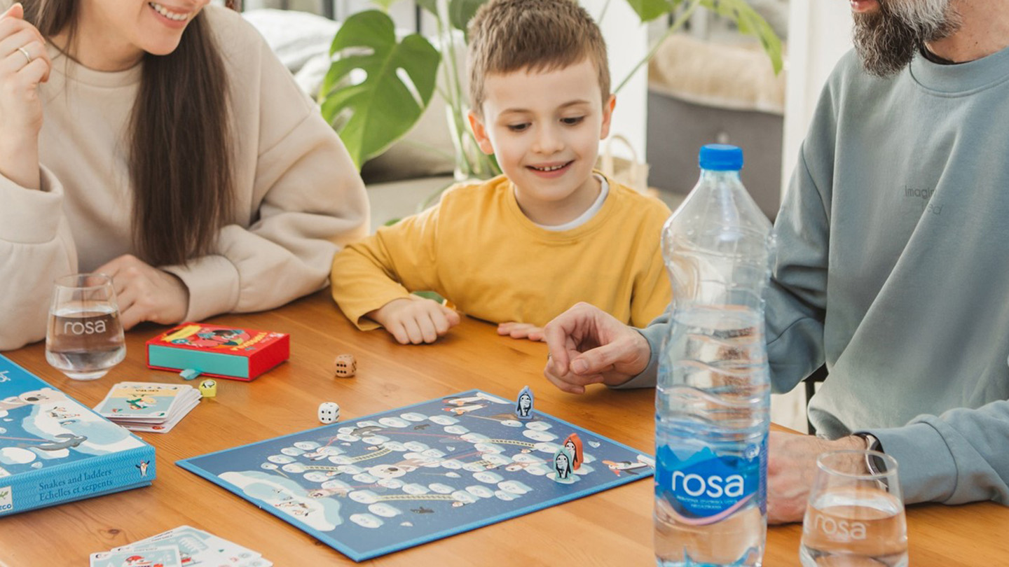 Familje luan lojë tavoline, në tavolinë ka shishe dhe gotë uji Rosa.