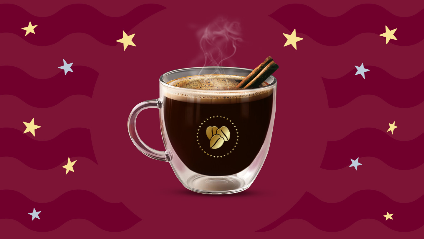 Una taza de cristal con café de olla caliente y dos varitas de canela sobre un fondo en tonos guinda.