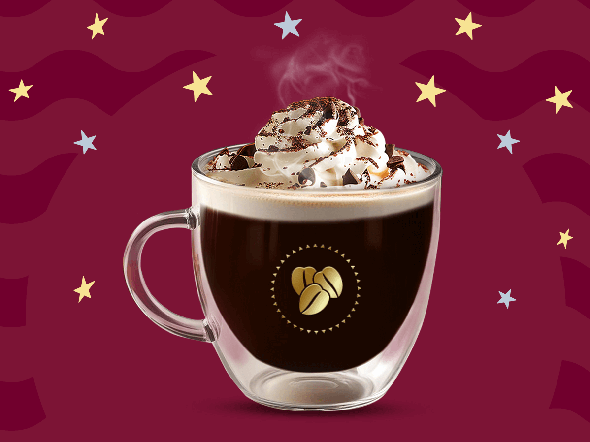 Una taza de cristal con café vienés caliente con crema batida por encima decorado con caco en polvo sobre un fondo en tonos guinda.