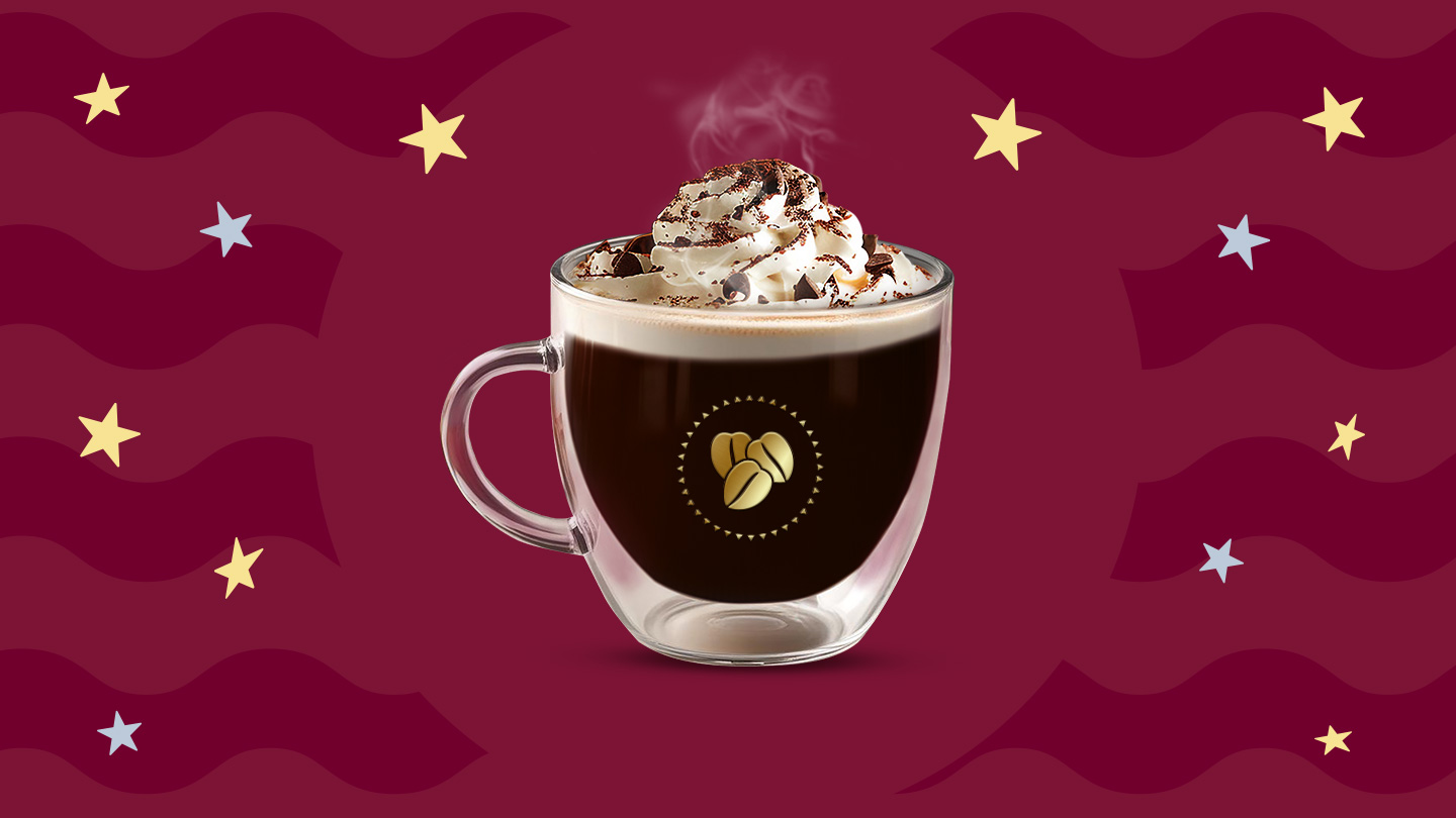 Una taza de cristal con café vienés caliente con crema batida por encima decorado con caco en polvo sobre un fondo en tonos guinda.