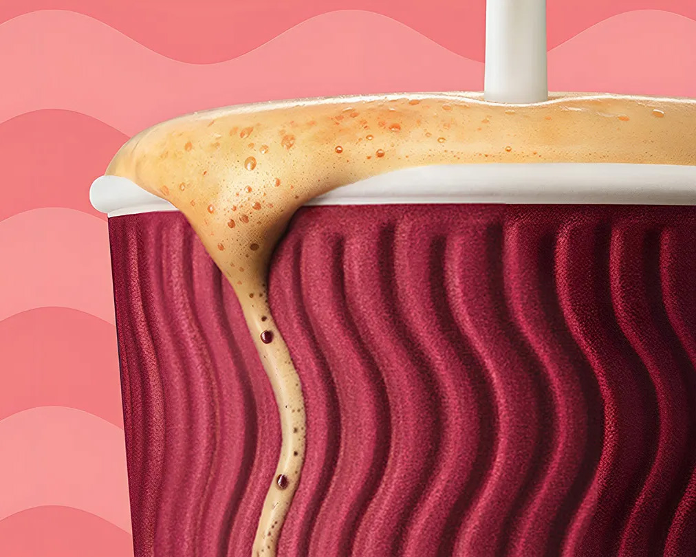 Chorro de leche cayendo sobre una vaso de café Costa Coffe para llevar sobre un fondo rosado.