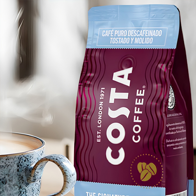 Paquete de café molido descafeinado Costa Coffe junto a una taza de café caliente.