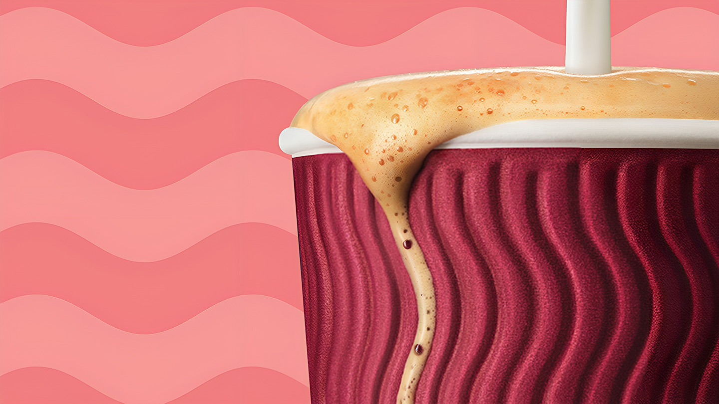 Chorro de leche cayendo sobre una vaso de café Costa Coffe para llevar sobre un fondo rosado.