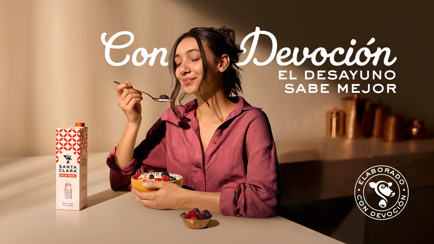 Mujer feliz desayunando con leche Santa Clara y el lema "Con Devoción".