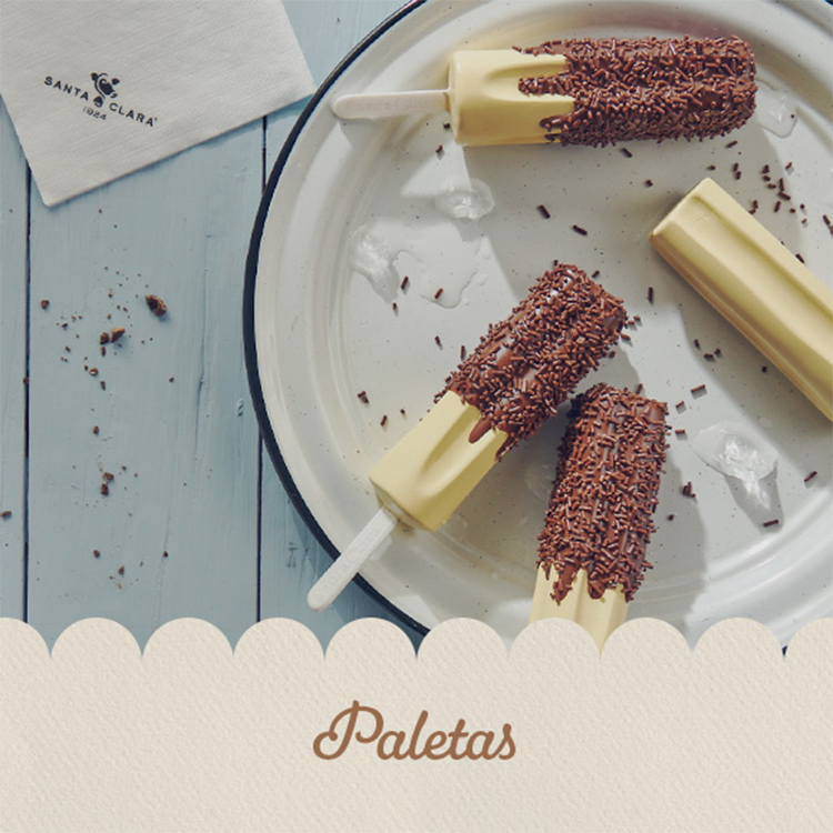 Paletas de helado bañadas parcialmente en chocolate y decoradas con chispas, servidas sobre un plato blanco con hielo.