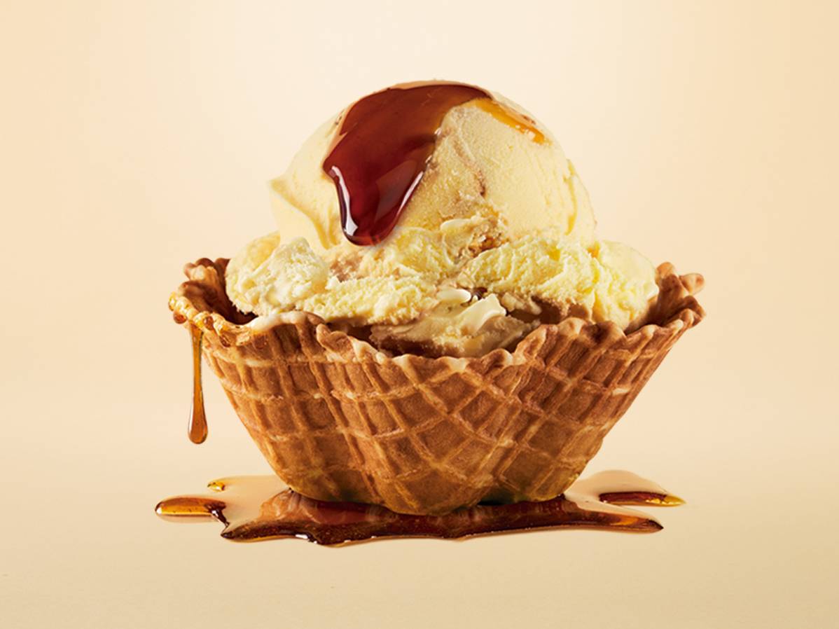 Imagen de una bola de helado Santa Clara, nuevo sabor, adornada con plátano, caramelo líquido y trozos de galleta. Se destaca el texto 'Nuevo Sabor' y el logo de Santa Clara.