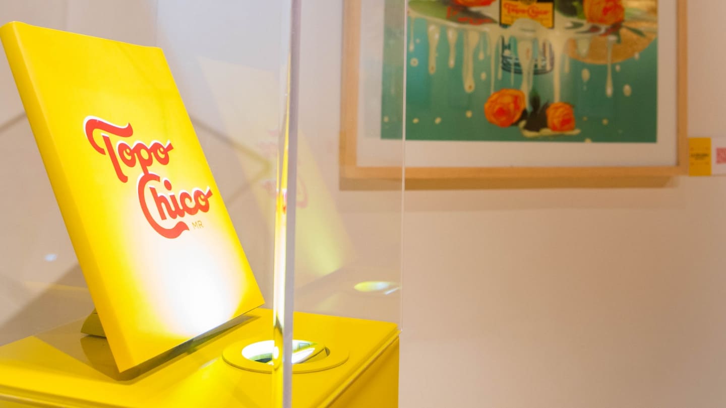Imagen de la exposición de una obra de arte, color amarillo con la frase Topo Chico