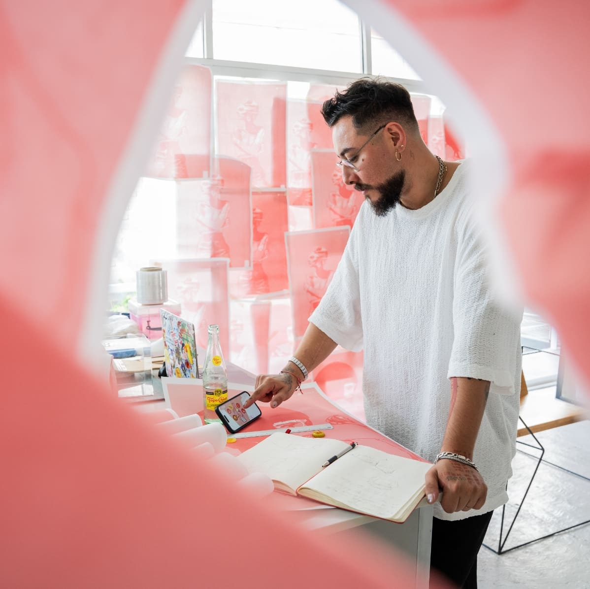 Diseñador parado en frente de un escritorio, usando su celular y con un marco rosa