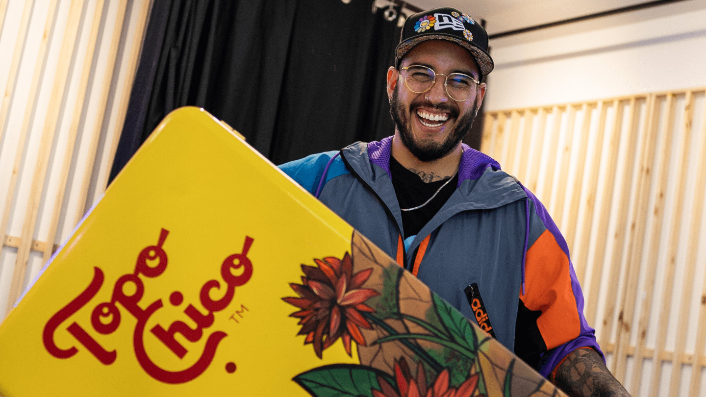 Diseñador sujetando una heladera Topo Chico de color amarillo y con dibujos de flores.