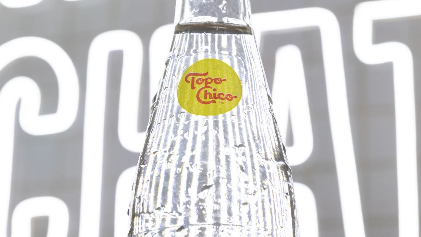 Primer plano de una botella de Topo Chico, sobre un fondo con letras de neón.